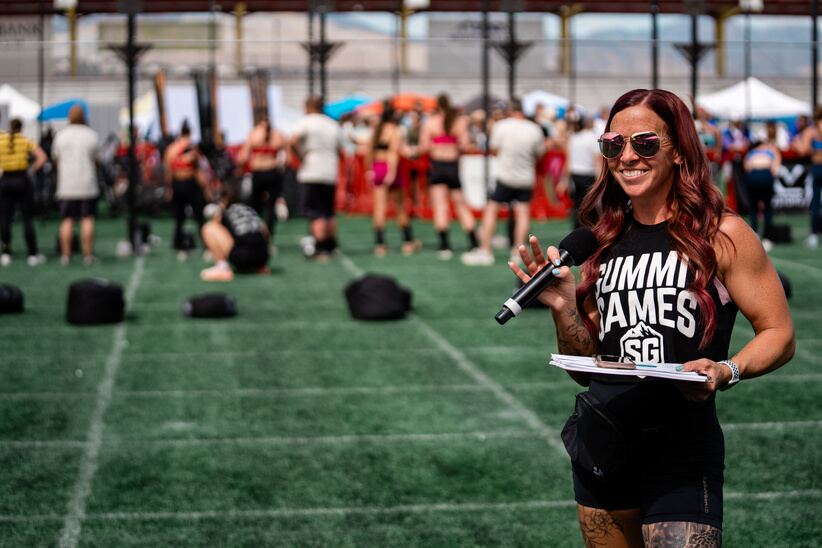 A coach with a microphone hosting a large outdoor fitness event on a turf field